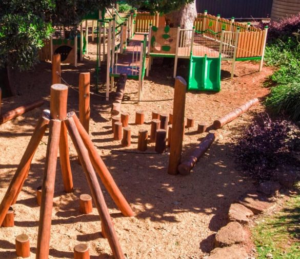 a playground with green slides and a wooden teepee